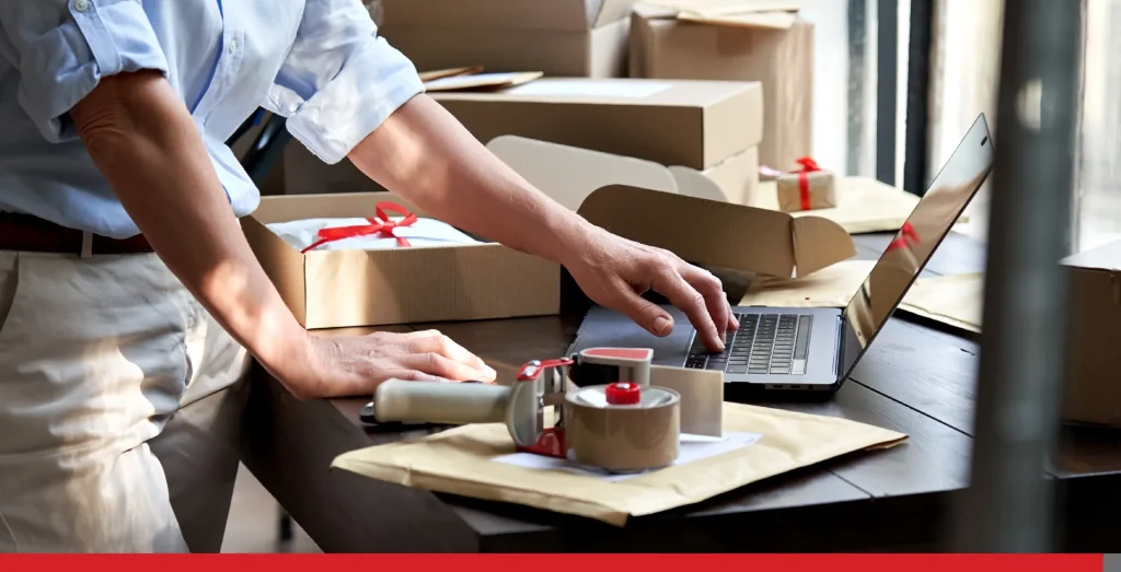 Person working on their laptop and packaging envelopes and boxes.