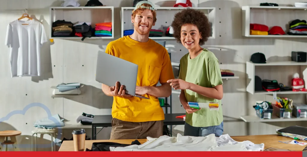 Positive young multiethnic craftspeople looking at camera while holding cloth swatches and laptop.