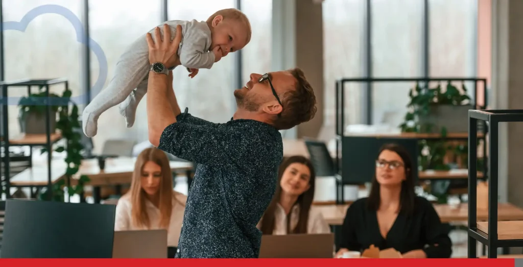 Bébé dans les bras d’un homme dans un bureau où un groupe de gens travaillent