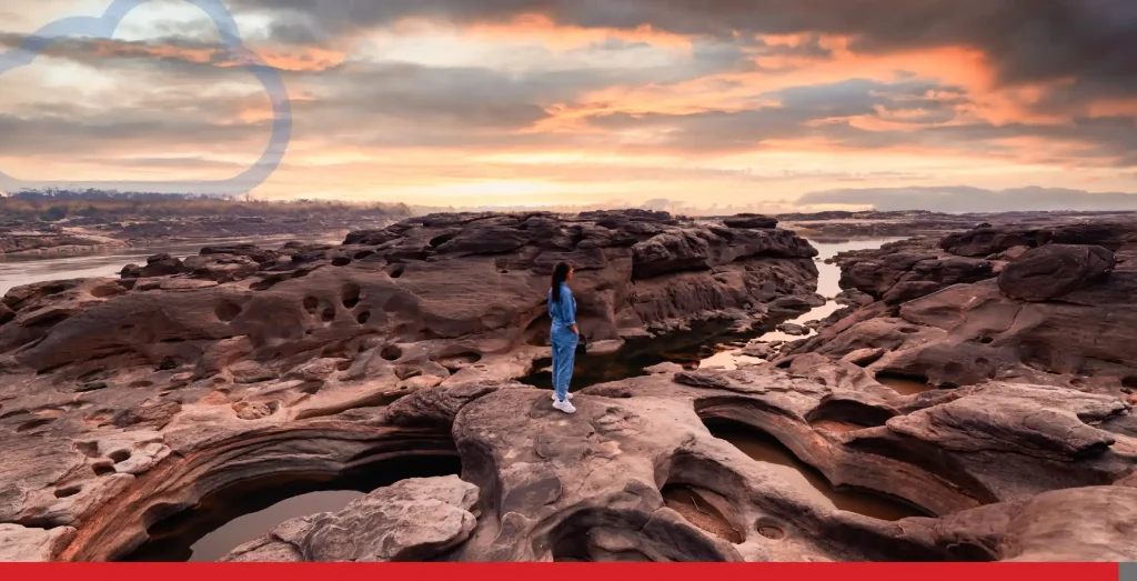 Woman traveler standing on eroded rocky rapids with Mekong river in the sunset at Sam Phan Bok.