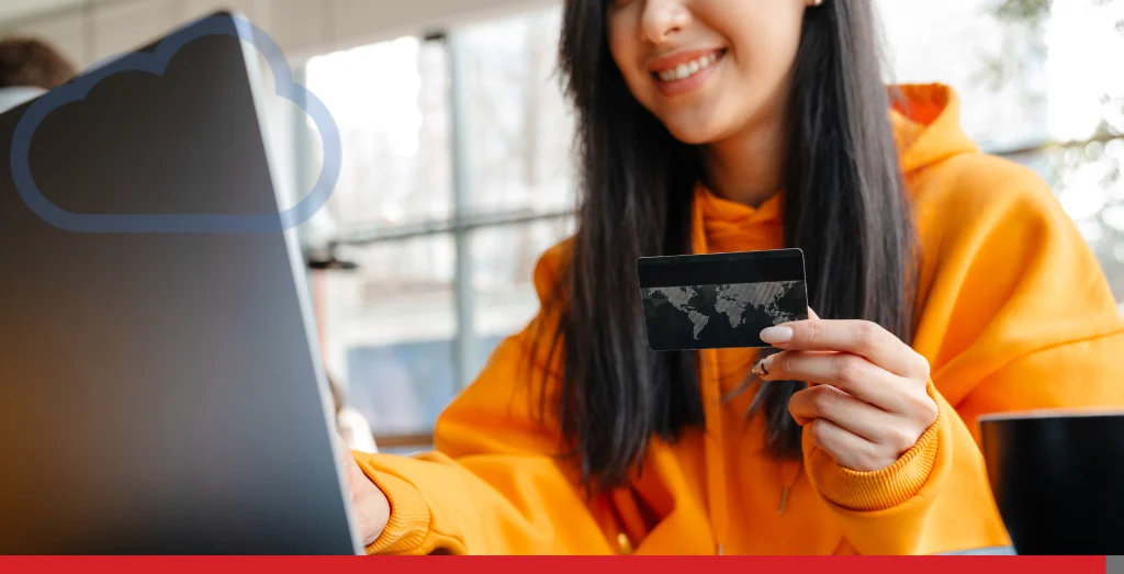 Smiling asian woman using credit card while working with laptop in cafe
